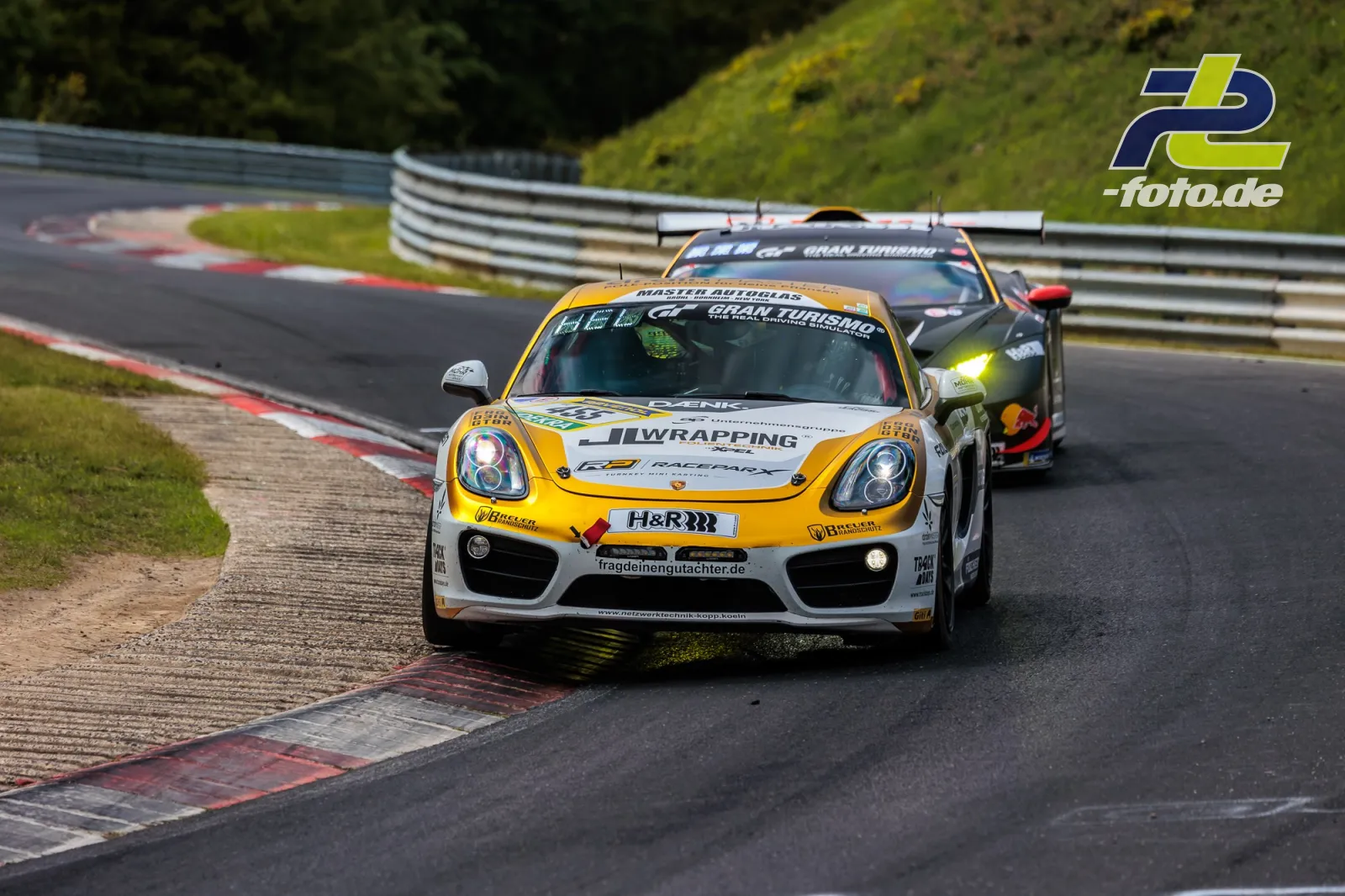 Porsche Cayman CM12 #455 des RSG SH e.V. in Kurve auf Nordschleife beim 24h-Rennen Nürburgring, gefolgt von weiterem Rennwagen.