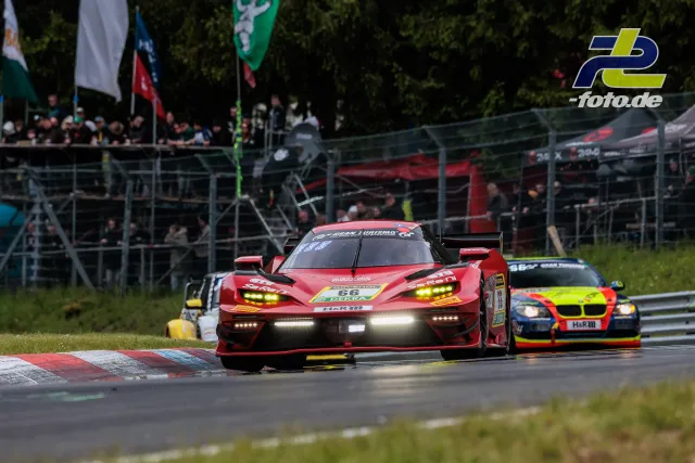 Roter Rennwagen 66 führt in einer Kurve am Nürburgring vor einem BMW, Zuschauertribüne im Hintergrund.