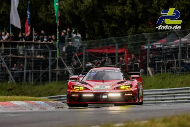 Dunkelroter GT-Rennwagen mit gelben Scheinwerfern auf der Nordschleife während des 24h-Rennens, Zuschauer im Hintergrund.