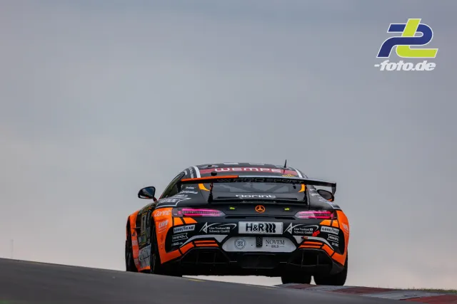 Mercedes-AMG GT3 in schwarz-oranger Lackierung über der Bergkuppe des Nürburgrings im Rennen.