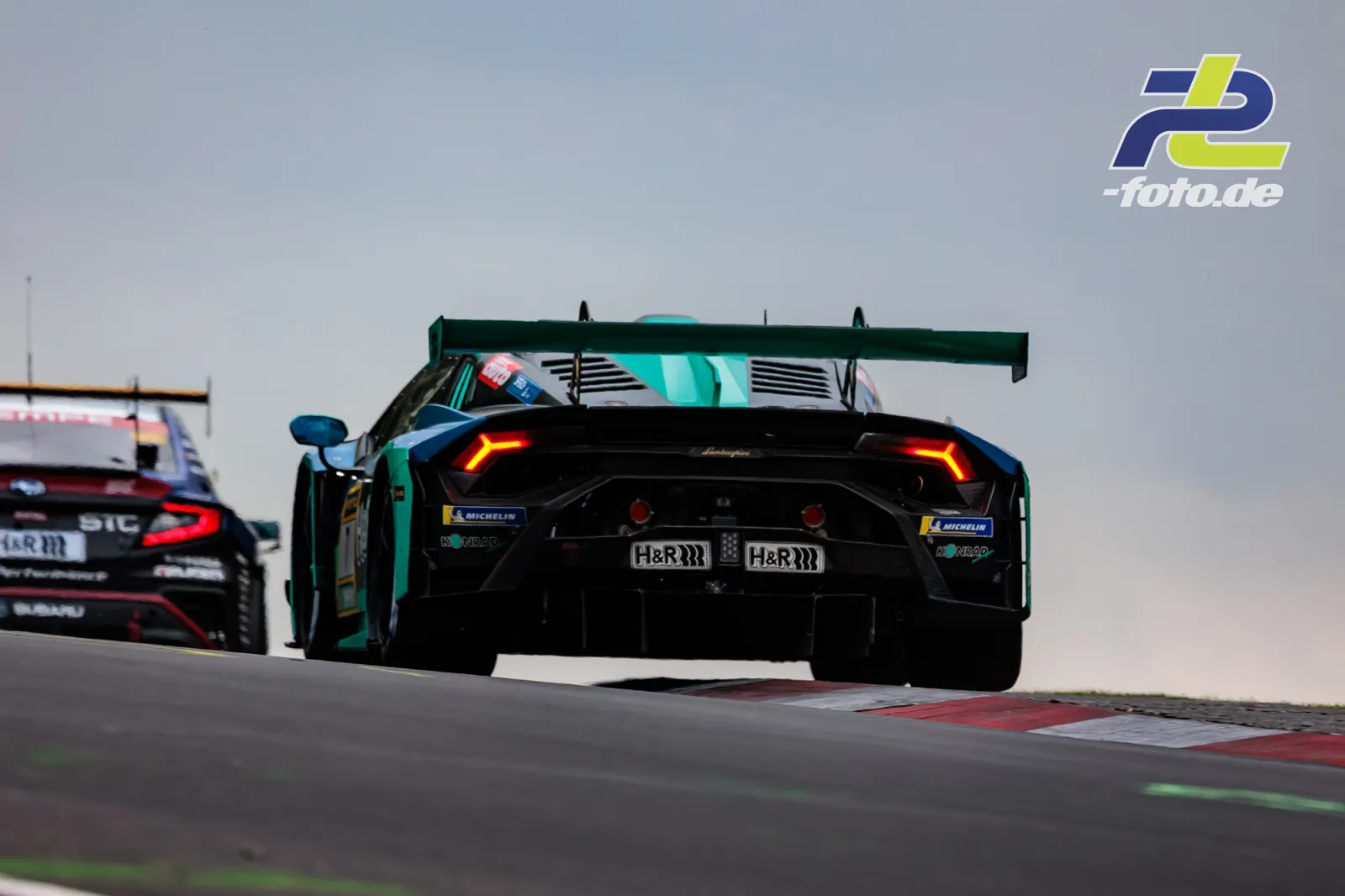 Lamborghini Huracán GT3 mit schwarzer Lackierung und türkisen Akzenten auf der Nordschleife, gefolgt von einem Porsche 911 GT3 R.