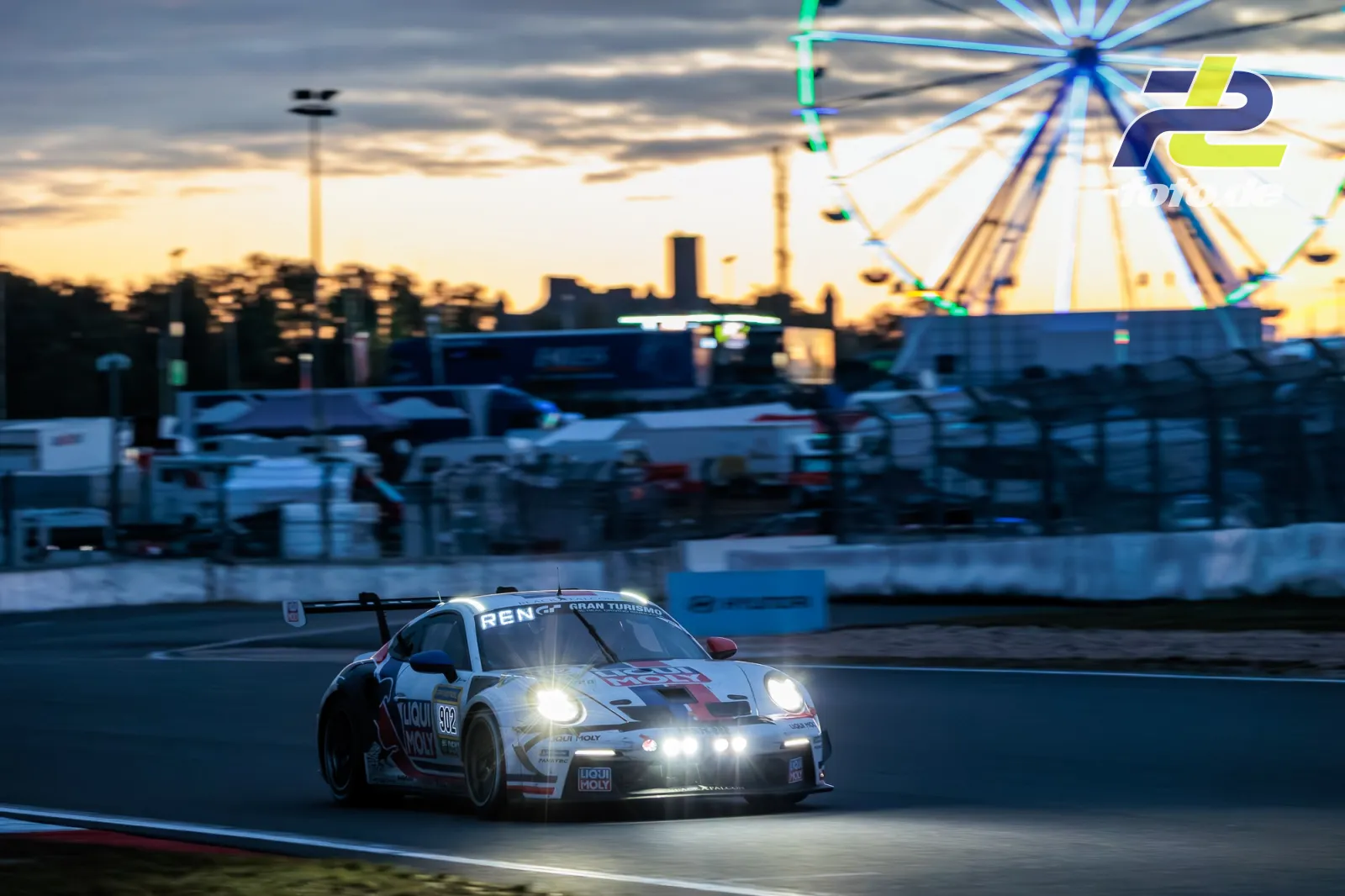 Porsche 911 GT3 Cup (992) mit eingeschalteten Scheinwerfern auf dem Nürburgring bei Dämmerung, im Hintergrund ein beleuchtetes Riesenrad.