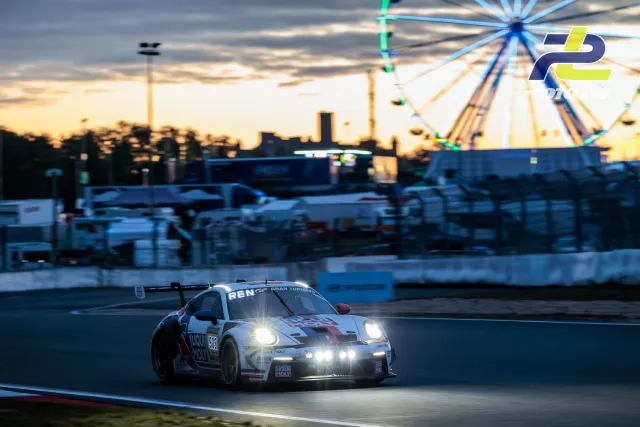 Porsche 911 GT3 R mit Scheinwerfern in der Abenddämmerung auf dem Nürburgring, Riesenrad im Hintergrund.