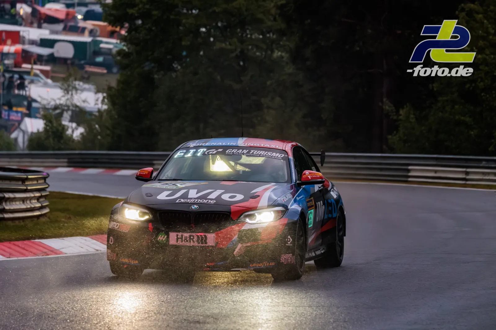 BMW M240i Racing Cup bei nassem Qualifying auf der Nürburgring-Nordschleife, Wassergischt aufwirbelnd, Scheinwerferlicht bei bedecktem Wetter.