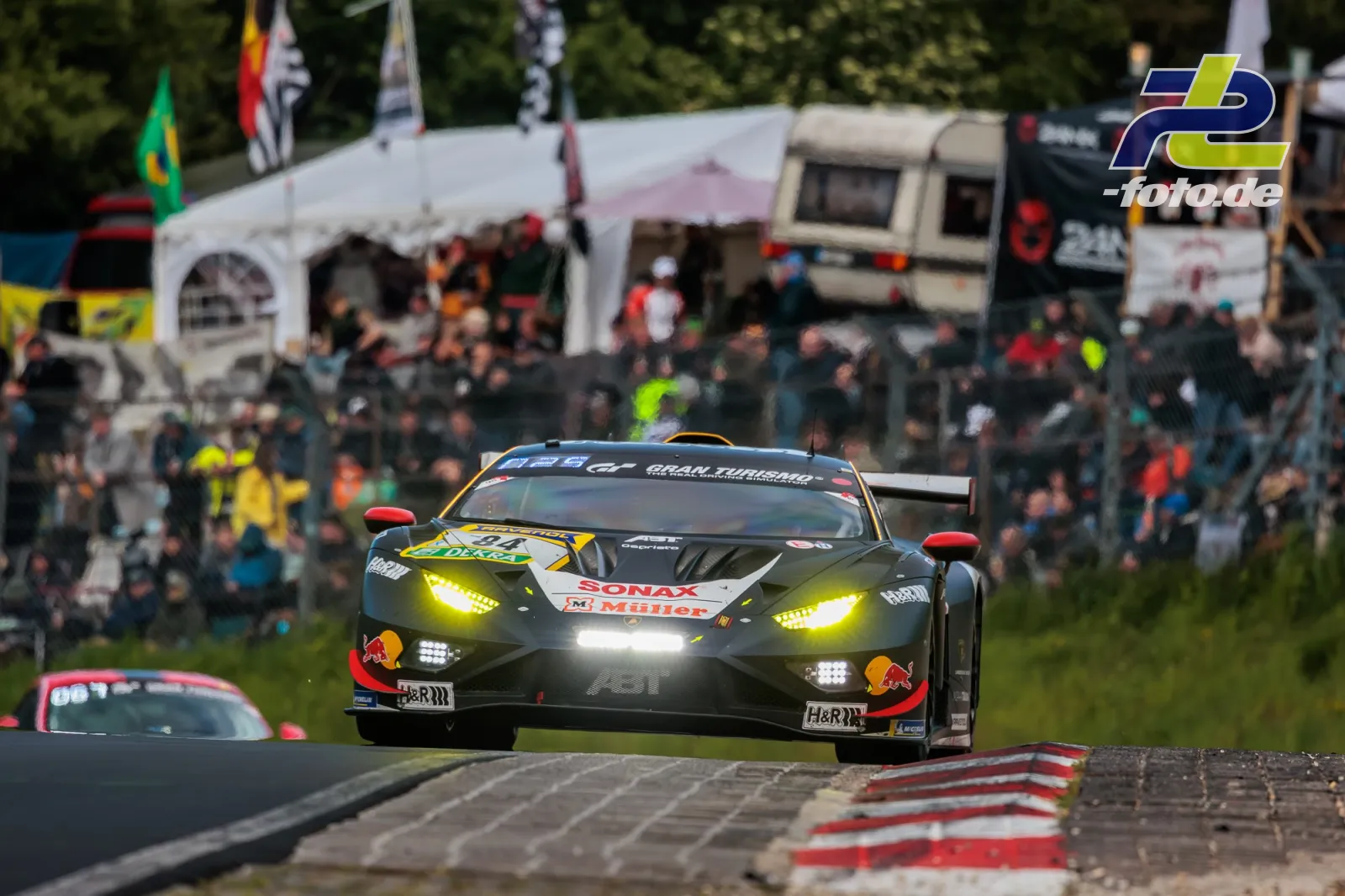 Lamborghini Huracán GT3 mit gelben Scheinwerfern auf der Nürburgring-Nordschleife vor Zuschauerkulisse während des 24h-Rennens.