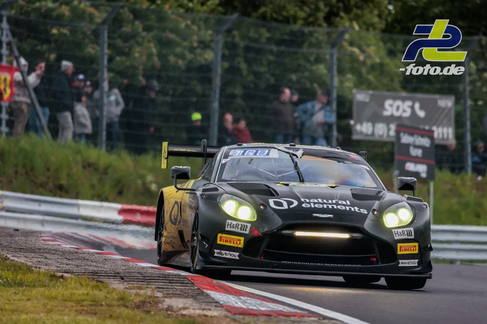 Aston Martin Vantage AMR GT3 EVO auf dem Nürburgring während des 24h-Rennens, über Randstein fahrend mit eingeschalteten Scheinwerfern.