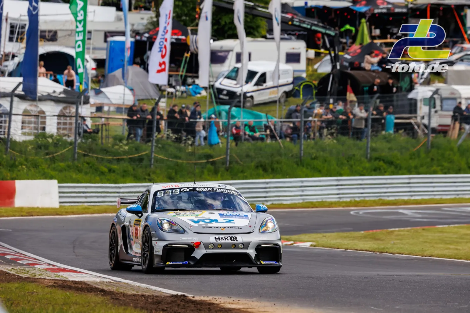 Porsche 718 Cayman GT4 Clubsport in Weiß-Blau im ersten Qualifying zum ADAC RAVENOL 24h Nürburgring, Fahrerlager im Hintergrund