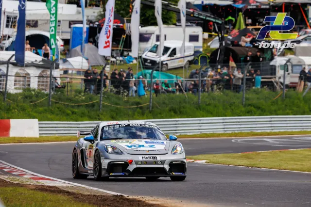 Porsche 718 Cayman GT4 Clubsport #979 in weiß-blau auf der Nordschleife beim Qualifying zum 24h-Rennen, Zuschauer im Hintergrund