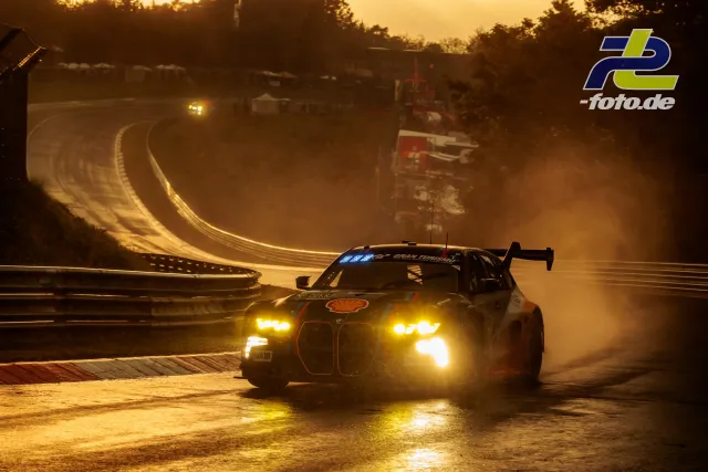 BMW M4 GT3 im Gegenlicht bei Sonnenuntergang auf der Nordschleife, dramatische Lichtstimmung mit eingeschalteten Scheinwerfern.