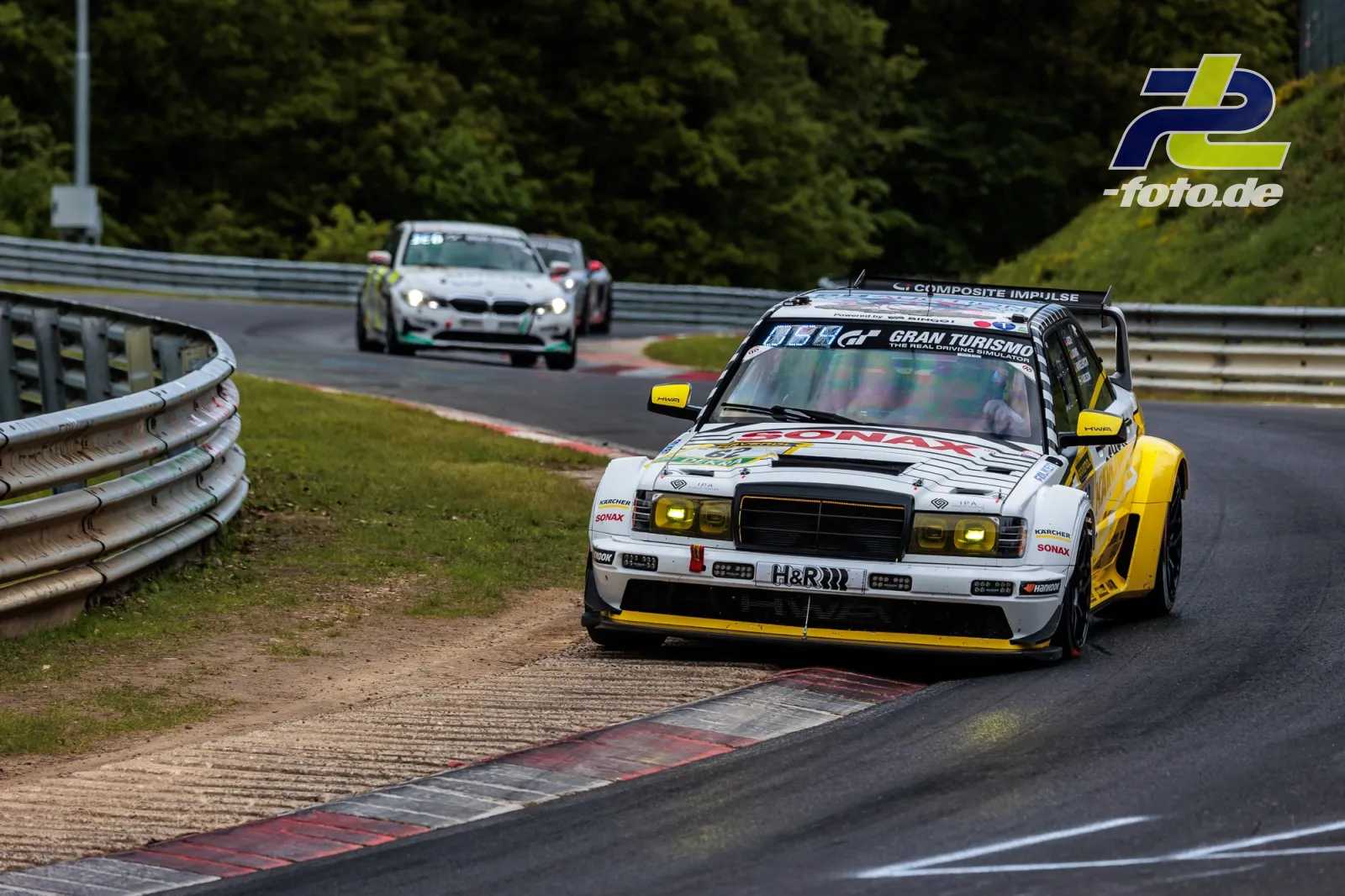 HWA Rennwagen in weiß-gelber Lackierung mit Gran Turismo Logo auf der Nordschleife, gefolgt von einem BMW, beim 24h-Rennen am Nürburgring.