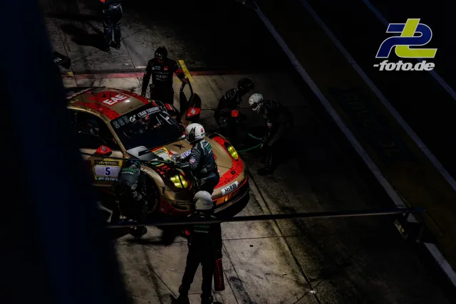 Boxenstopp bei Nacht während des 24h-Rennens am Nürburgring, Porsche 911 GT3 R (992) Evo26 mit Startnummer 5 in rot-gold, Mechaniker arbeiten am Fahrzeug.