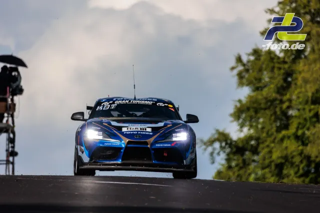 Toyota GR Supra GT4 EVO2 #170 bei der Fahrt über eine Kuppe beim 24h-Rennen Nürburgring, frontal mit eingeschalteten Scheinwerfern.