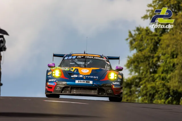 Porsche 911 GT3 R in Blau-Orange mit eingeschalteten Scheinwerfern beim 24h-Rennen am Nürburgring über eine Kuppe springend.
