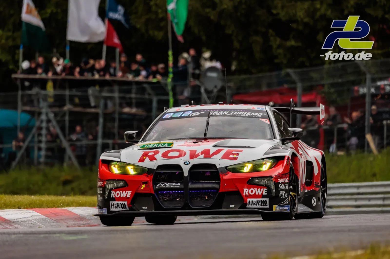 BMW M4 GT3 EVO von ROWE RACING in frontaler Fahraufnahme auf dem Nürburgring beim 24h-Rennen, Zuschauer im Hintergrund.