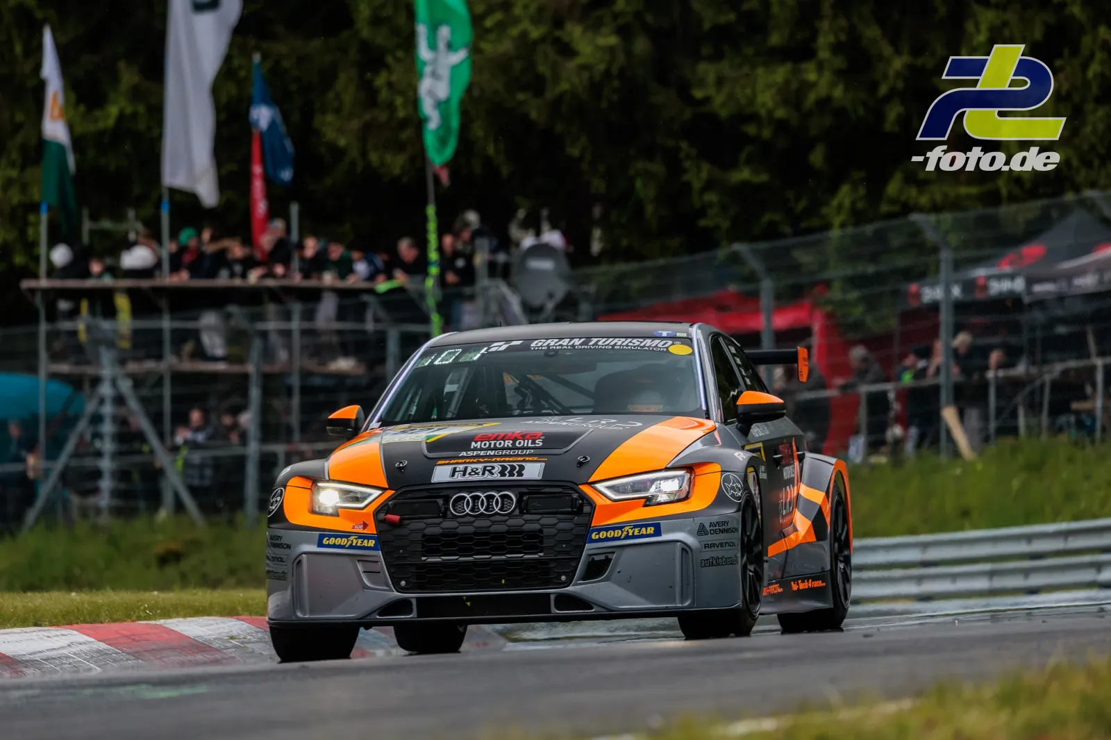 Audi RS3 LMS DSG mit Startnummer 821 in Kurve beim 24h-Rennen Nürburgring, orange-graue Lackierung, Zuschauer im Hintergrund.