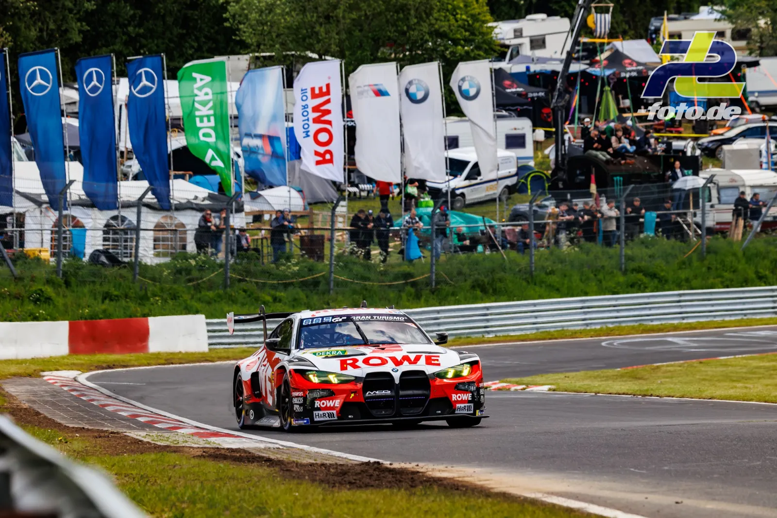 BMW M4 GT3 von ROWE Racing im Qualifying auf der Nürburgring-Nordschleife, Zuschauerbereich mit Sponsorenfahnen im Hintergrund