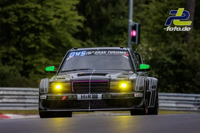 Mercedes-Benz 190 E mit Chromlackierung und Startnummer 049 im Rennen beim 24h-Rennen Nürburgring mit leuchtenden gelben Scheinwerfern.
