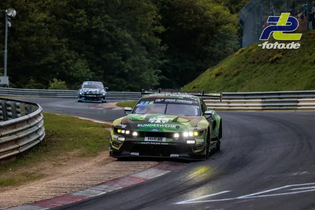 Ford Mustang GT3 in grün-gelber Bundeswehr-Lackierung auf der Nordschleife im Rennen, zweites Fahrzeug im Hintergrund.