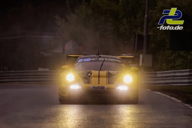 Porsche 911 GT3 R auf nasser Strecke bei Dämmerung mit eingeschalteten Scheinwerfern während des Qualifyings am Nürburgring.