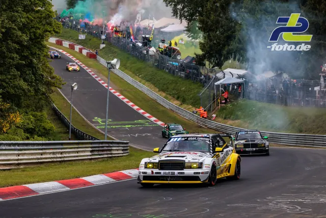 HWA EVO.R mit weiß-gelber Lackierung auf der Formationsrunde auf dem Nürburgring, dahinter GT3-Fahrzeuge, Zuschauer mit Rauchfackeln.
