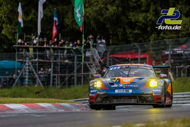 Porsche 911 GT3 R im GT Invest-Design auf der Nordschleife des Nürburgrings während des 24h-Rennens mit Zuschauertribüne im Hintergrund
