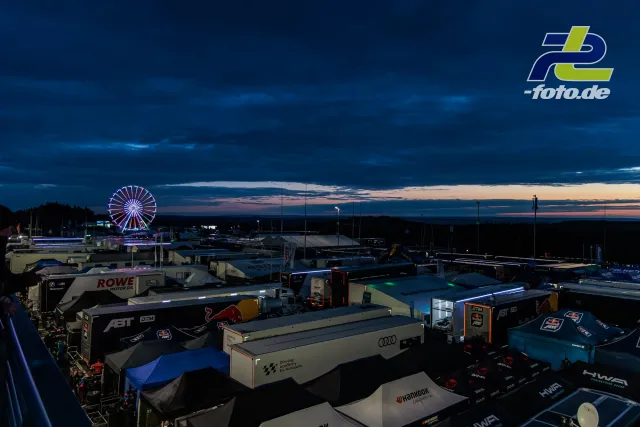 Fahrerlager am Nürburgring in der Dämmerung während des 24h-Rennens, beleuchtetes Riesenrad im Hintergrund