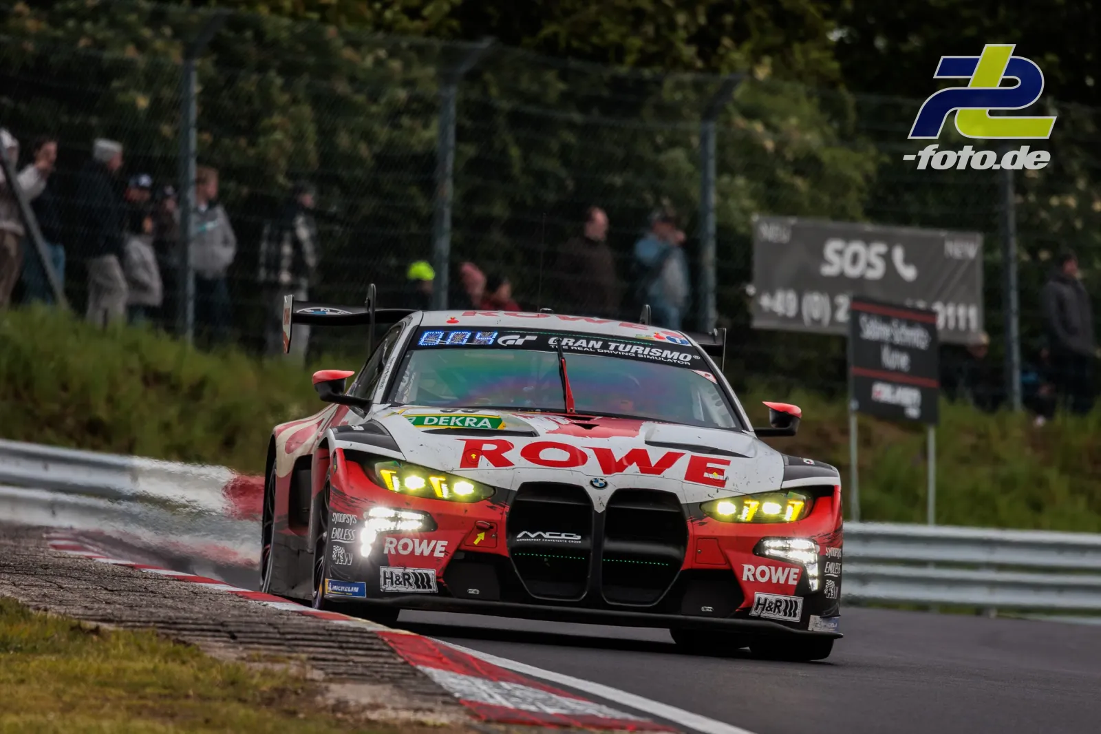 BMW M4 GT3 von ROWE Racing in Kurve auf nasser Strecke beim 24h-Rennen Nürburgring, Zuschauer im Hintergrund