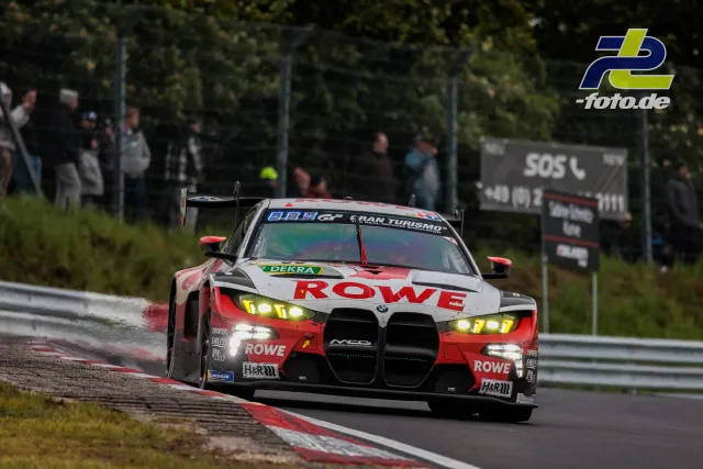 BMW M4 GT3 von ROWE Racing in Kurve auf nasser Strecke beim 24h-Rennen Nürburgring, Zuschauer im Hintergrund