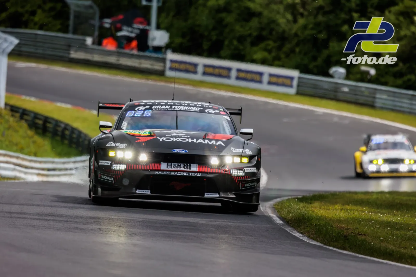 Ford Mustang GT3 des Haupt Racing Teams mit schwarz-roter Lackierung in Kurvenausfahrt, gefolgt von weiterem Fahrzeug auf der Nordschleife.