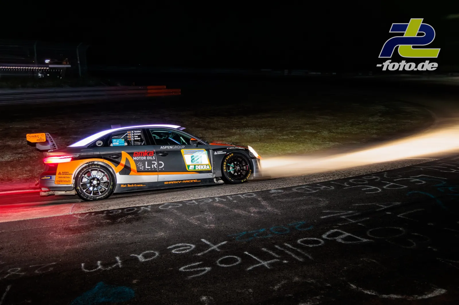 Rennwagen fährt nachts auf der Nordschleife, leuchtende Bremsscheiben und Scheinwerfer sichtbar.