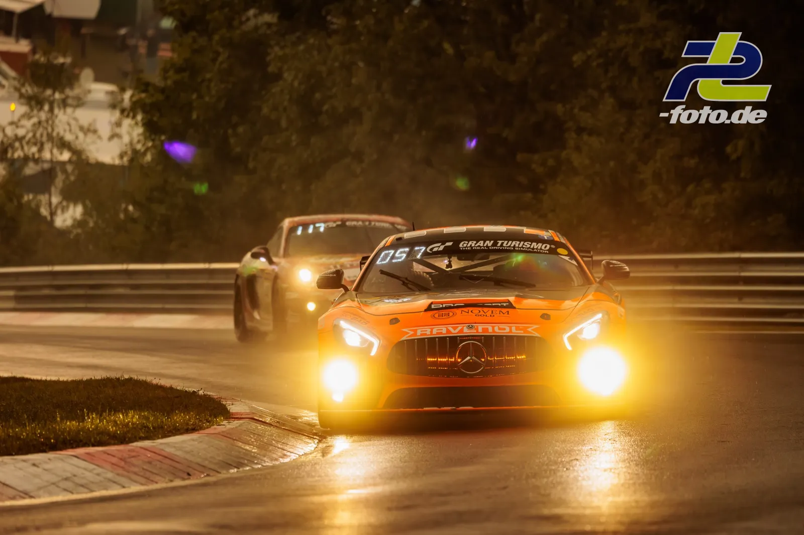 Zwei GT-Fahrzeuge bei der Nürburgring-Qualifikation im goldenen Abendlicht, führendes Auto in Orange mit eingeschalteten Scheinwerfern.