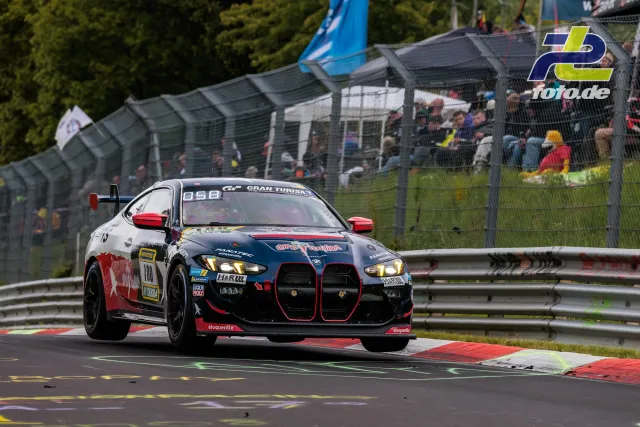 BMW M4 GT3 #110 in dunkelblau-roter Lackierung während des 24h-Rennens auf dem Nürburgring, Zuschauer am Streckenrand.