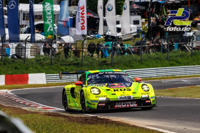 Neongelber Porsche 911 GT3 R #911 mit Red Bull und Veltins Sponsoring in Kurve auf Nordschleife, Tribünen mit Zuschauern im Hintergrund.