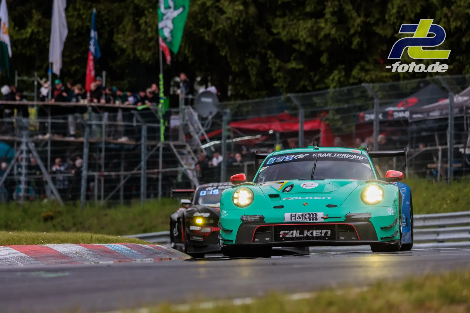 Porsche 911 GT3 R in türkis fährt auf nasser Strecke vor Zuschauertribüne während des 24h-Rennens am Nürburgring.