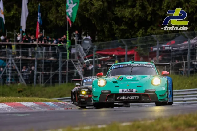Türkiser Porsche 911 GT3 R mit Falken-Lackierung wird vor Zuschauertribüne im Rennen verfolgt, Nürburgring 24h.