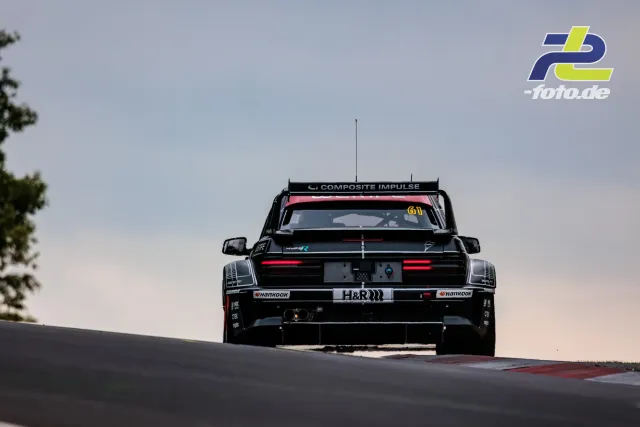 Schwarzer Rennwagen mit Startnummer 61 über einer Kuppe am Nürburgring, Heckansicht mit großem Heckspoiler im Gegenlicht.
