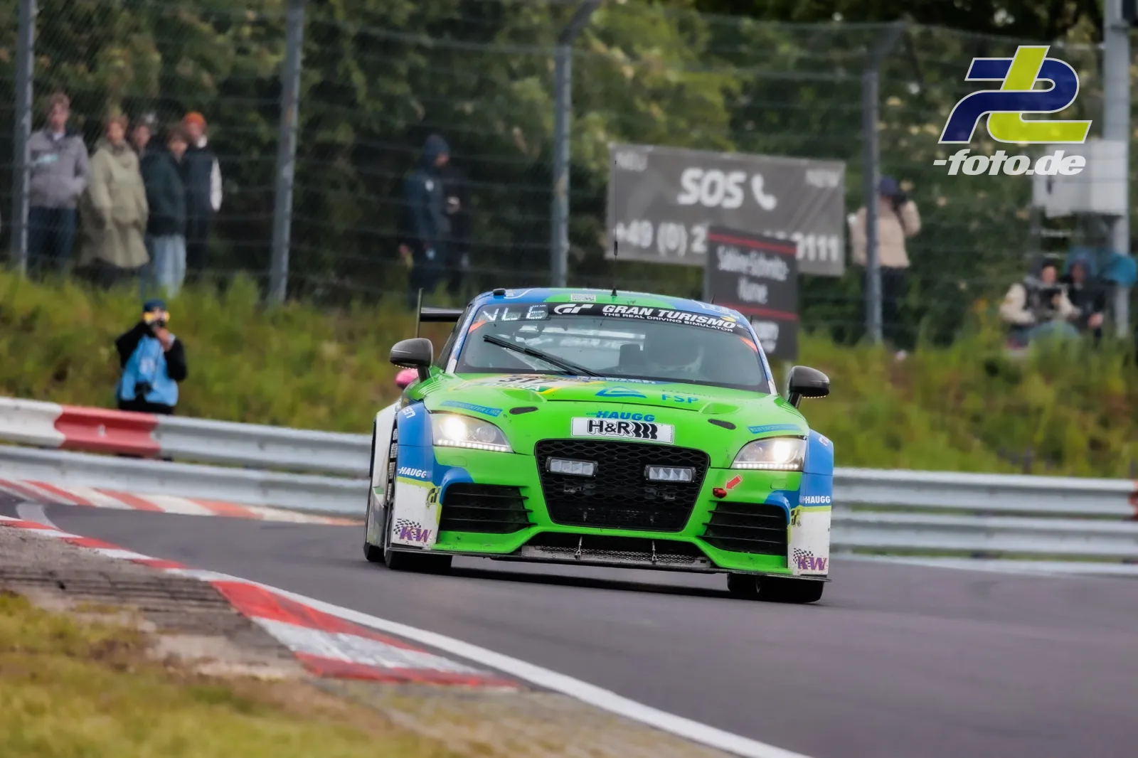 Grün-blauer Audi TT auf der Nürburgring-Nordschleife beim 24-Stunden-Rennen, Zuschauer hinter dem Zaun.