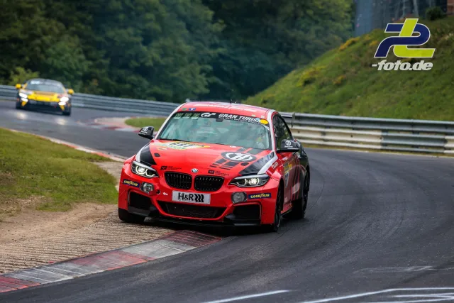 Roter BMW M240i Racing nutzt auf der Nordschleife Randsteine, gelbes GT-Fahrzeug im Hintergrund.