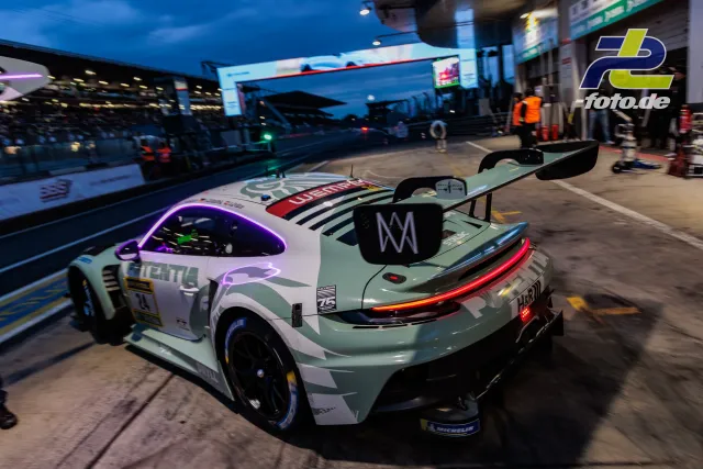 Porsche 911 GT3 R in mintgrüner und weißer Lackierung mit Startnummer 75 in der Boxengasse während der blauen Stunde.