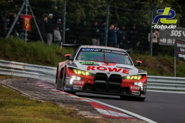 BMW M4 GT3 von ROWE Racing in Kurve auf der Nürburgring-Nordschleife mit Zuschauern im Hintergrund während des 24h-Rennens.