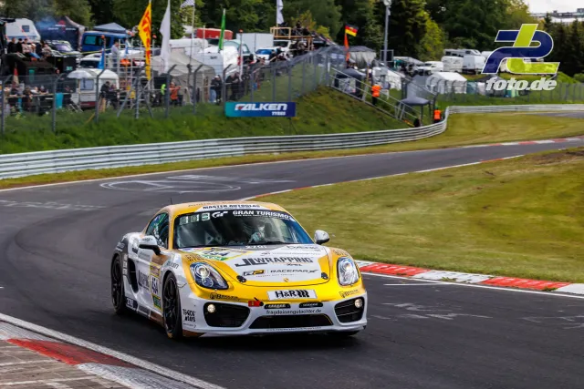 Porsche Cayman in weiß-gelber Lackierung auf der Nürburgring-Nordschleife während des Qualifyings, Zuschauer im Hintergrund.