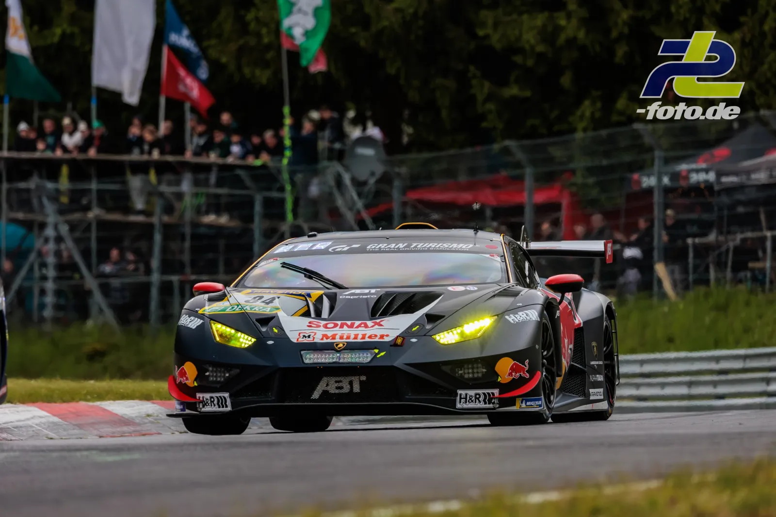 Lamborghini Huracán GT3 auf der Nordschleife beim 24h-Rennen Nürburgring mit eingeschalteten Scheinwerfern vor Zuschauerrängen.
