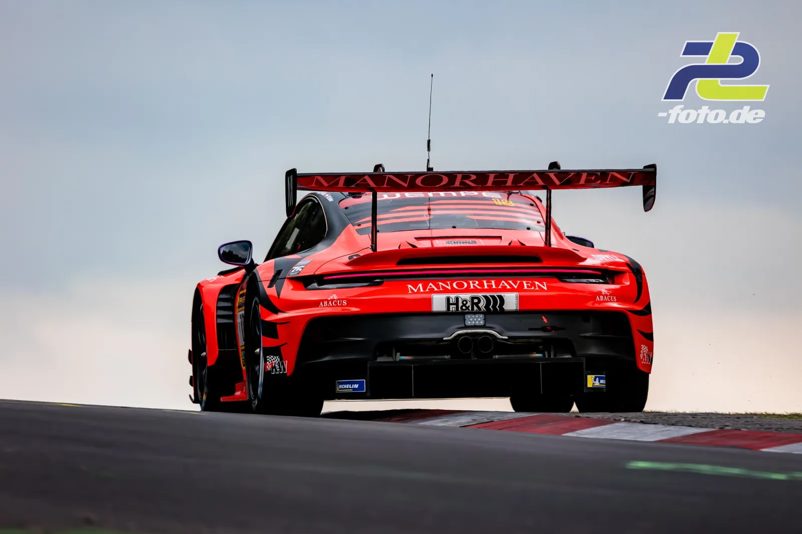 Roter Porsche 911 GT3 R mit Manorhaven-Lackierung von hinten in einer Kurve am Nürburgring während des 24h-Rennens.