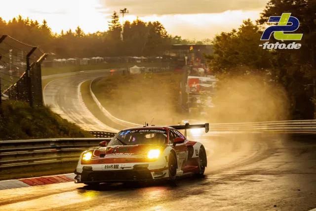 Porsche 911 GT3 R in rot-weißer Lackierung auf nasser Nürburgring-Nordschleife im Gegenlicht mit Gischt während des Qualifyings.