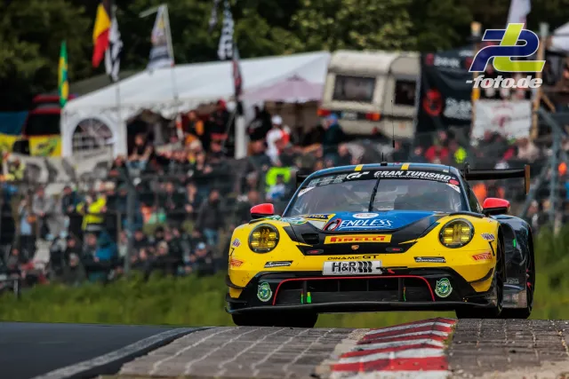 Porsche 911 GT3 R in gelb-schwarz-blauer Lackierung fährt über Randstein auf der Nordschleife beim 24h-Rennen Nürburgring