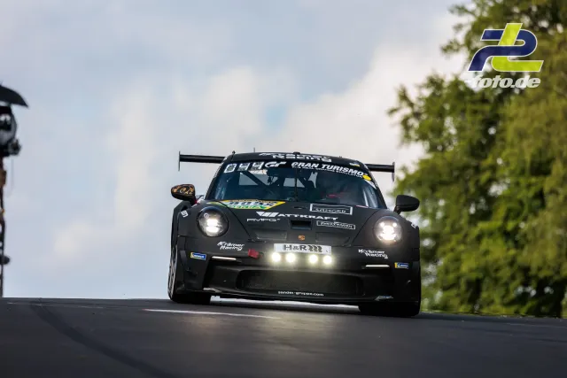 Schwarzer Porsche 911 GT3 R springt über eine Kuppe auf der Nürburgring-Nordschleife während des 24h-Rennens mit eingeschalteten Scheinwerfern.