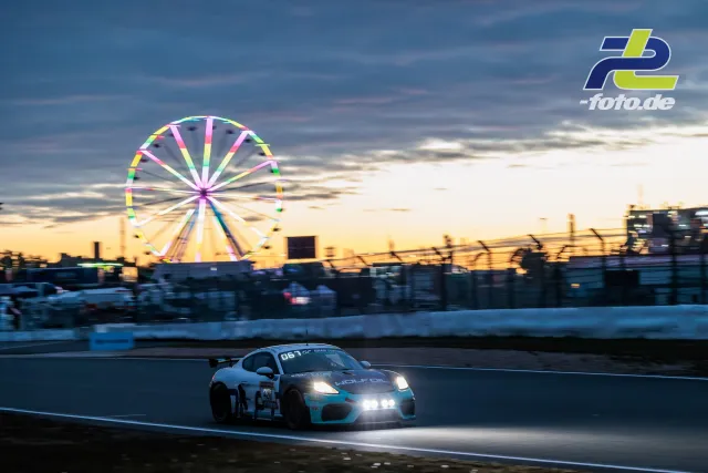 Porsche 718 Cayman GT4 mit Startnummer 420 bei Dämmerung auf dem Nürburgring, Riesenrad im Hintergrund während des 24h-Rennens.