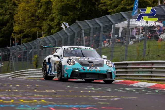 Porsche 911 GT3 R #7 in türkis-weißer Wolf-Lackierung während des 24h-Rennens auf dem Nürburgring, Zuschauer im Hintergrund