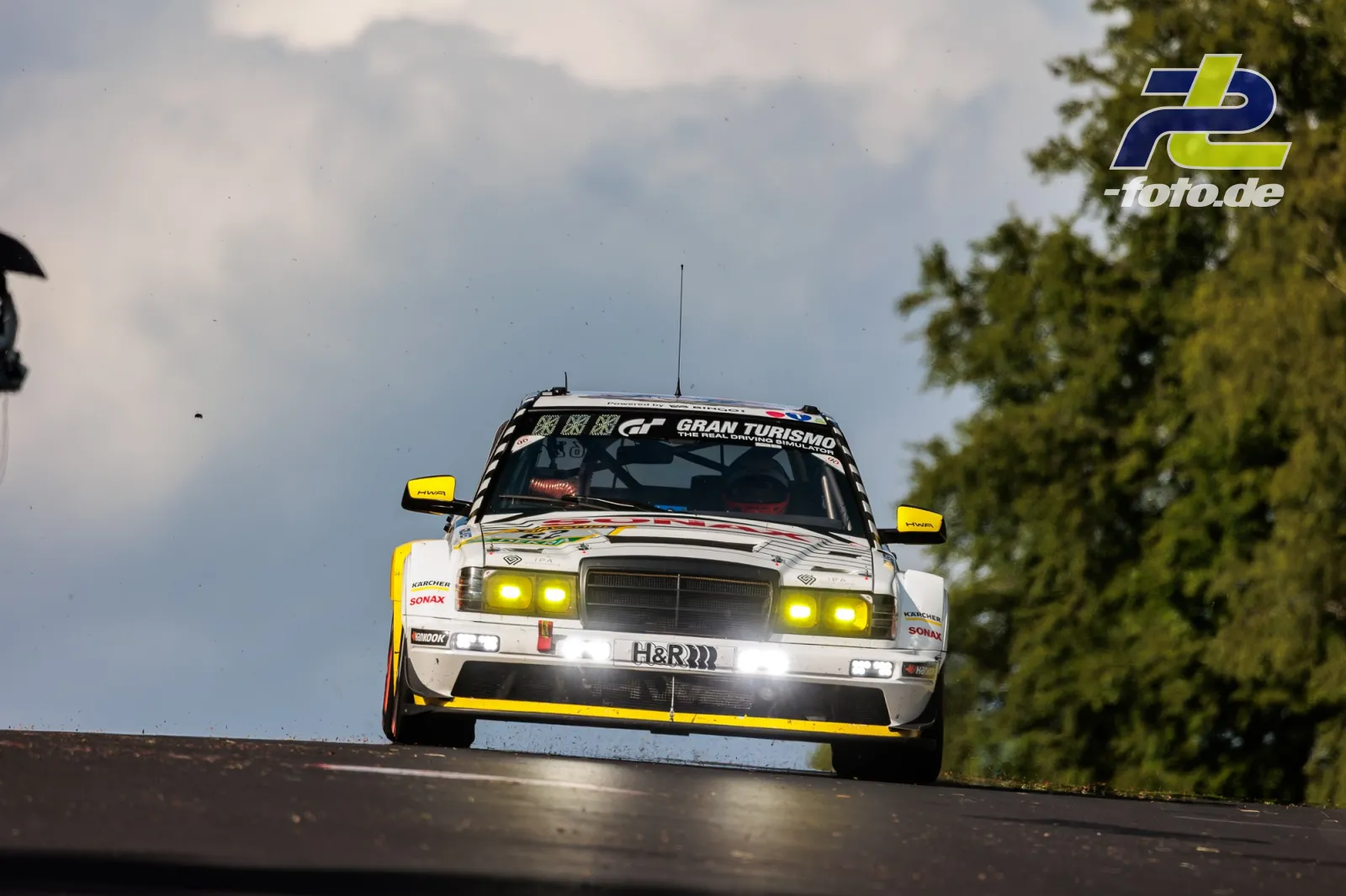 HWA EVO.R in Sprungphase mit gelben Spiegelkappen und eingeschalteten Scheinwerfern auf der Nordschleife beim 24h-Rennen Nürburgring.