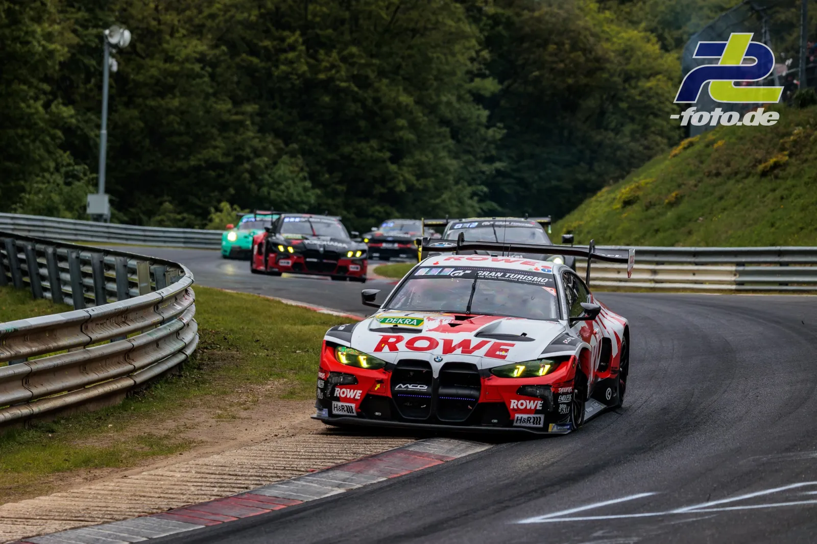 BMW M4 GT3 EVO des Teams ROWE RACING in Kurve auf dem Nürburgring, gefolgt von mehreren GT3-Fahrzeugen während des 24h-Rennens.